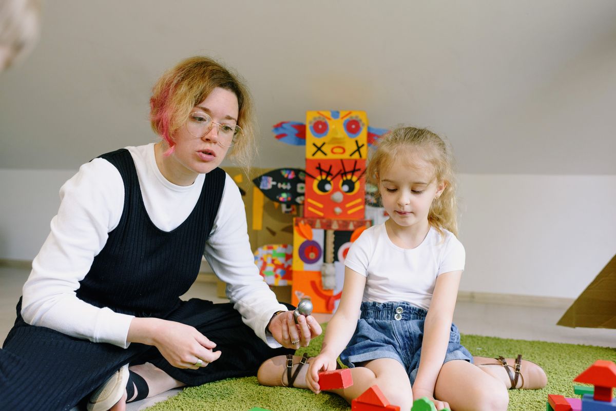 A therapist and young girl building together with colorful wooden blocks