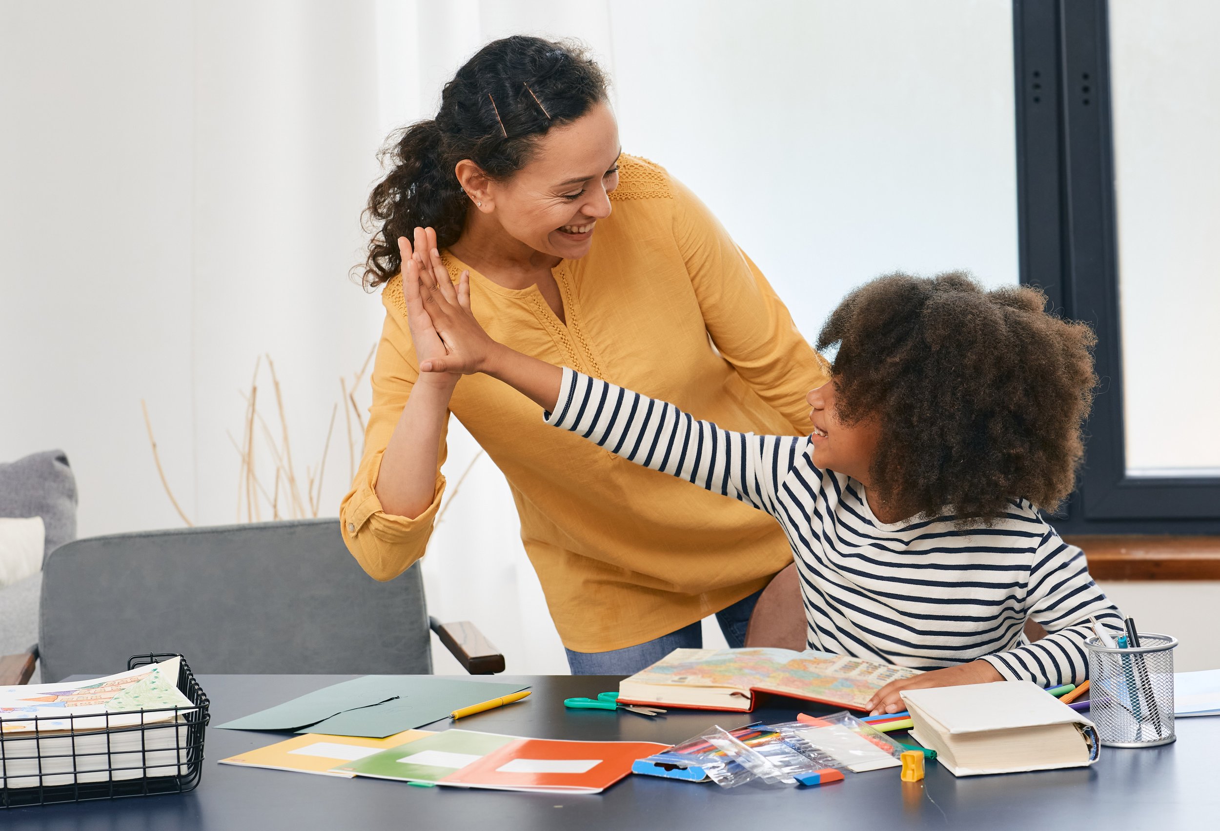 A caregiver and a young child sharing a high five during a learning activity at home